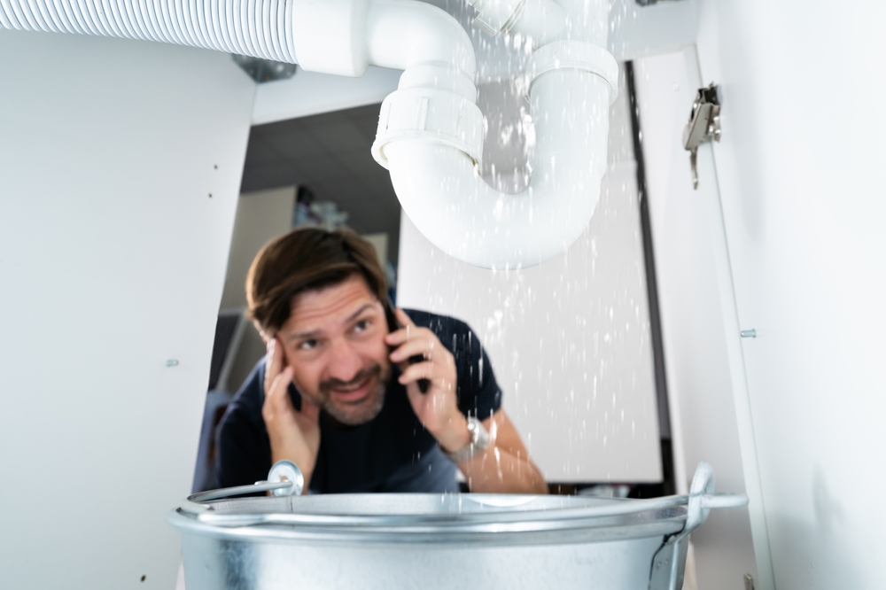 Man calling plumber while watching water leaking from sink